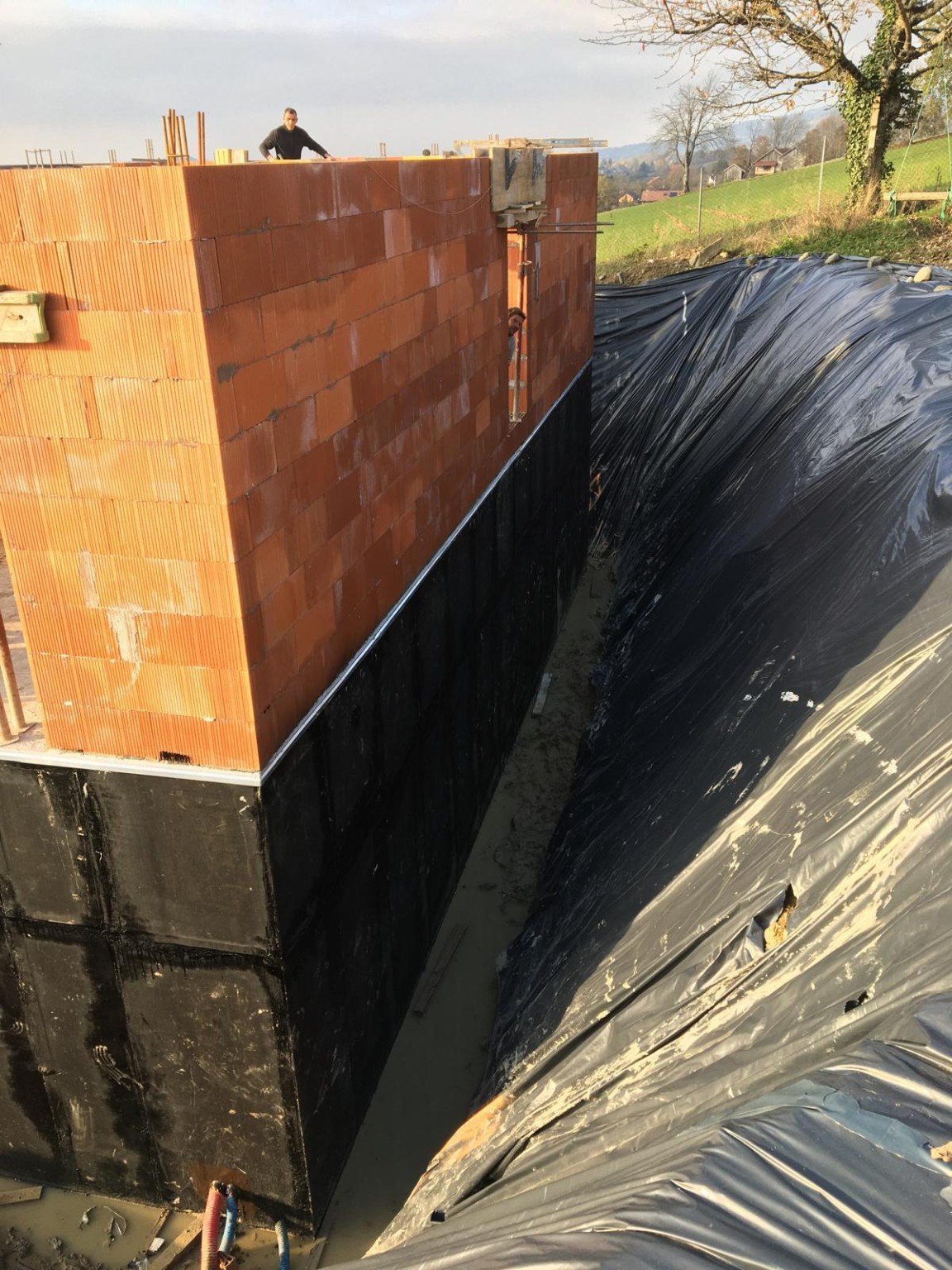 Membrane noire sur les parois enterrées d’un bâtiment en briques, avant remblaiement
